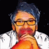 a man with glasses and a beard is sitting down with his hands on his chin .