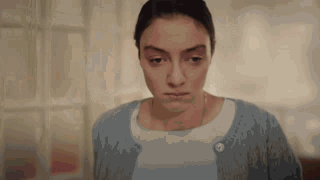a woman in a blue sweater looks down with a sad look on her face