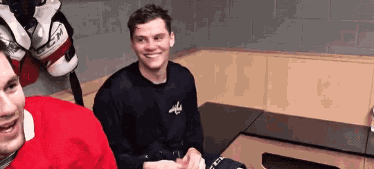 two hockey players are sitting in a locker room smiling and laughing .