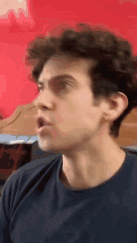 a close up of a man 's face with his mouth open in front of a red wall .