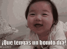 a baby is smiling and laying on a bed with the words `` que tengas un bonito dia ! ''