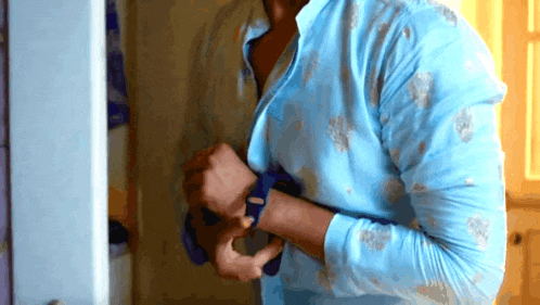 a man in a blue shirt is putting on a blue tie