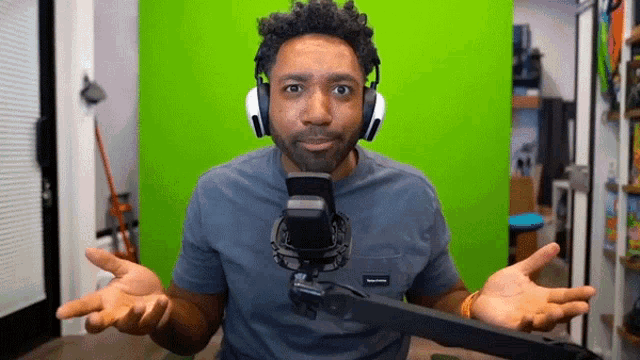 a man wearing headphones is sitting in front of a green screen and talking into a microphone .