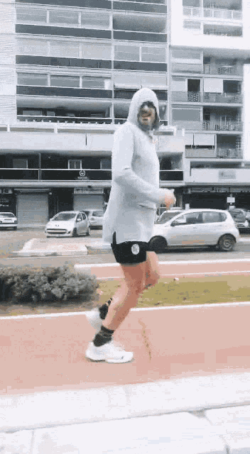 a man wearing a hoodie and shorts is jogging on a sidewalk