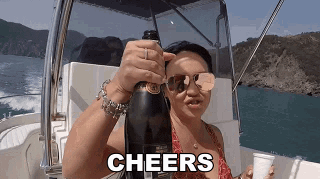 a woman on a boat is holding a bottle of champagne and the word cheers is above her