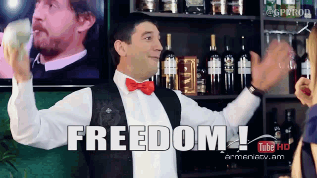 a man in a bow tie stands in front of a shelf with bottles of alcohol and says freedom on the bottom