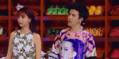 a man and a woman are standing next to each other in front of a shelf with fruits and vegetables .