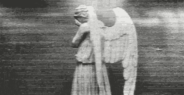 a black and white photo of a statue of an angel covering her face with her hand .