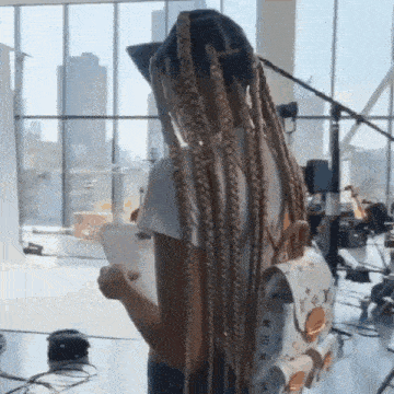 a woman with dreadlocks is standing in front of a large window holding a cup of coffee .