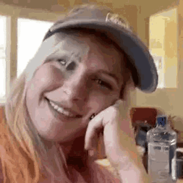 a woman wearing a baseball cap is smiling and talking on a cell phone .