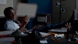 a man is sitting at a desk in a dark room reading a newspaper .