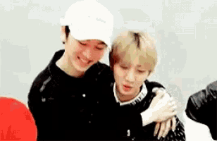 two young men are hugging each other in a room . one of the men is wearing a white hat .