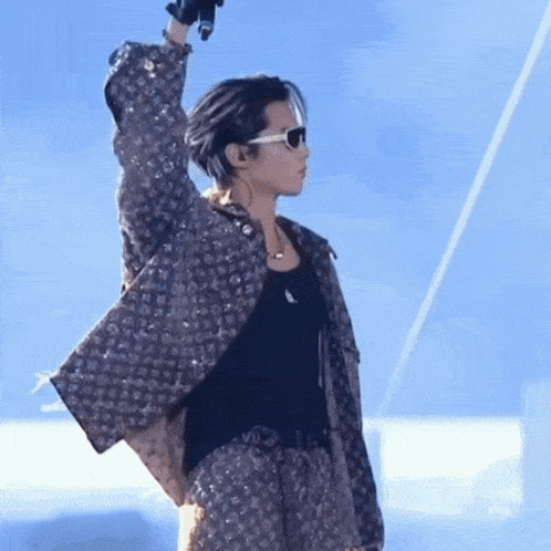 a man wearing sunglasses and a louis vuitton jacket is holding a microphone in his hand .