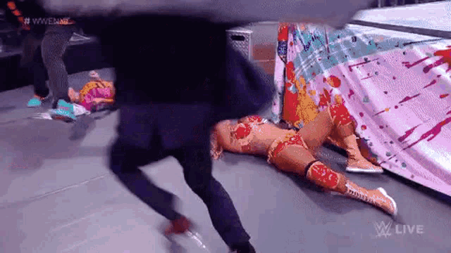 a wrestler is laying on the ground while a man kicks her in the face .