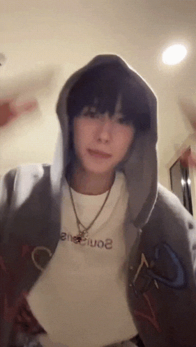 a young man wearing a hoodie and a necklace is standing in a room .