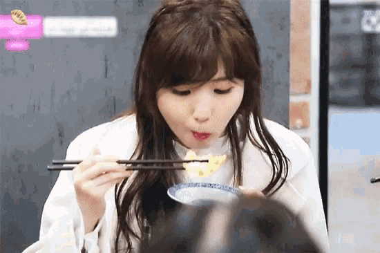 a woman is eating food with chopsticks in front of a wall with a sign that says ' a ' on it