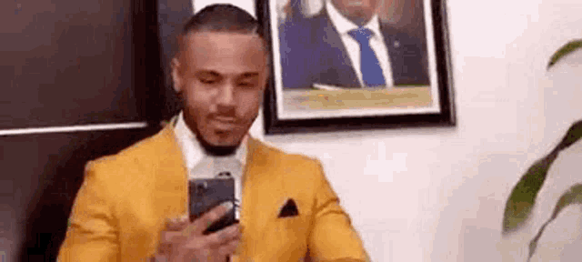 a man in a yellow suit and tie is looking at his phone .