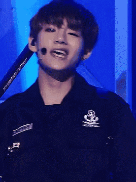 a young man is wearing a black jacket and holding a microphone while singing into it .