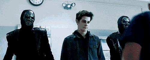 a man in a black jacket is standing next to two masked men in a room with a clock on the wall .