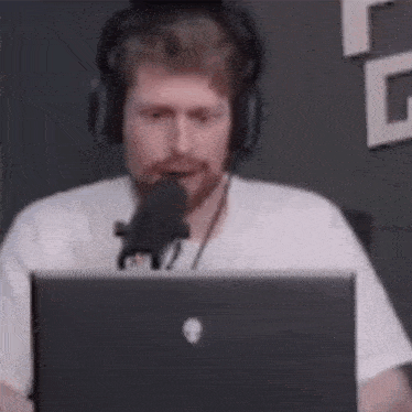 a man wearing headphones is talking into a microphone while sitting in front of a laptop computer .