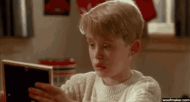 a young boy in a sweater is looking at a picture frame