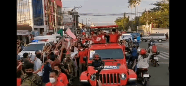 a crowd of people are gathered around a red jeep that says team on the front .