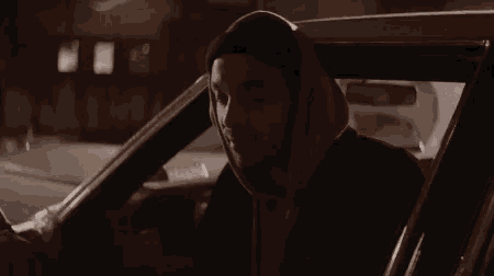 a man in a hoodie is sitting in a car with the words les gars sont bout written below him .