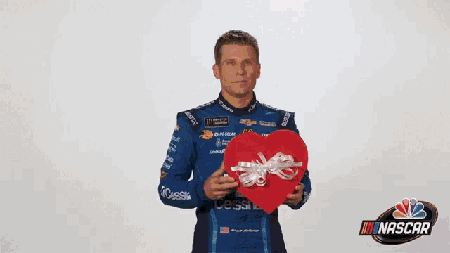 a nascar driver is holding a red heart in his hands