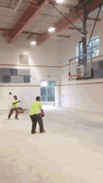 two men are playing basketball in a gym and one is wearing a yellow shirt