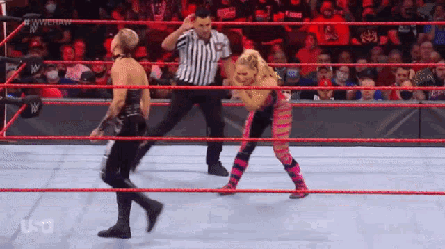 a man and a woman are wrestling in a wrestling ring with a referee in the background .