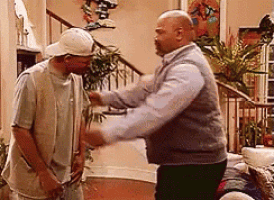 two men are standing next to each other in a living room in front of a staircase .