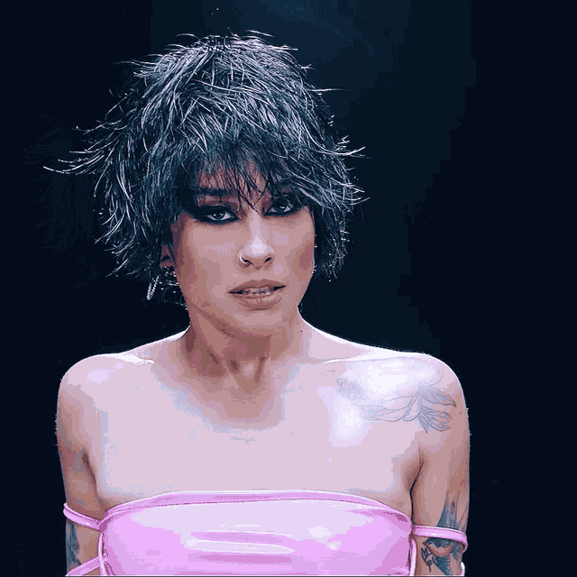 a woman wearing a wig and a pink top has a tattoo on her shoulder