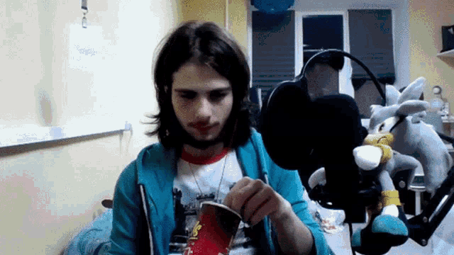 a man is holding a cup in front of a microphone with a stuffed animal behind him