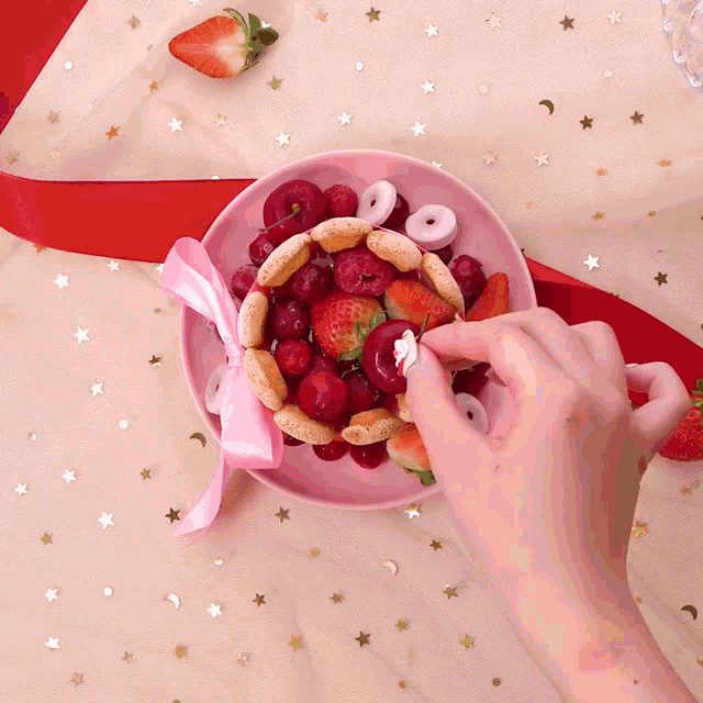 a bowl of strawberries and cherries with a pink bow on it