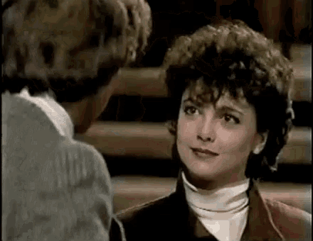 a man and a woman are looking at each other . the woman is wearing a turtleneck and a jacket .