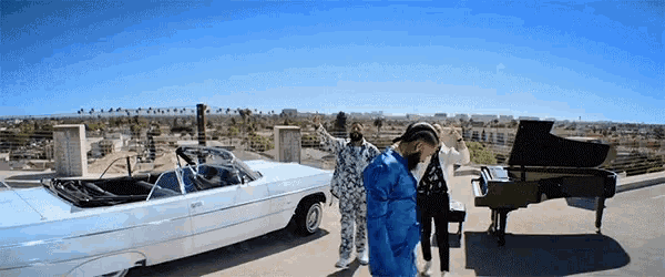 a man in a blue jacket stands next to a piano and a car