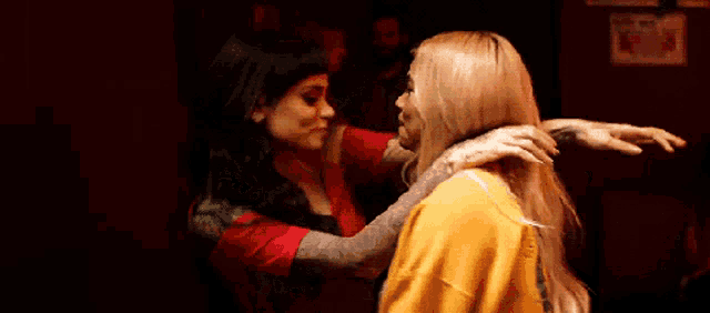 two women are kissing in a dark room and one is wearing a yellow sweater