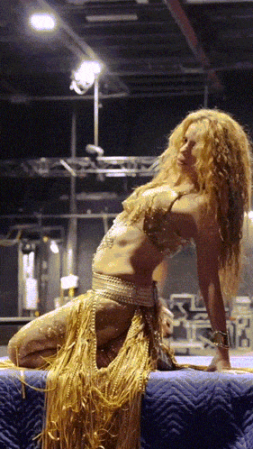 a woman in a gold costume is kneeling on a blue blanket