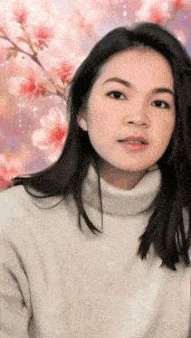 a woman wearing a white turtleneck sweater stands in front of a pink background with flowers