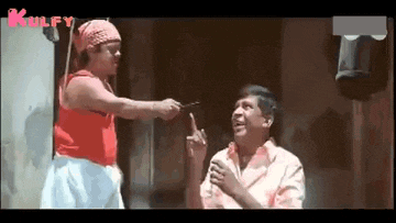 a man is pointing at another man while holding a pair of scissors in his hand .