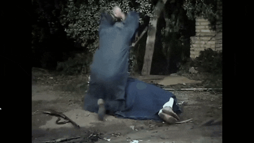 a man in a blue jacket is standing next to a woman in a blue dress laying on the ground .