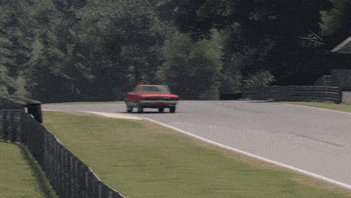 a red car is driving down a road with a fence in the foreground
