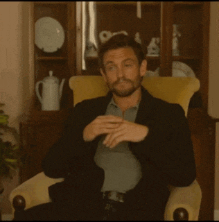 a man in a suit is sitting in a chair with his hands folded