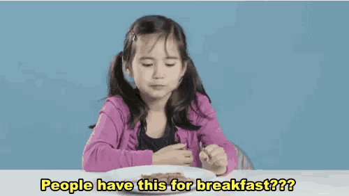 a little girl is sitting at a table with a plate of food and asking people have this for breakfast .