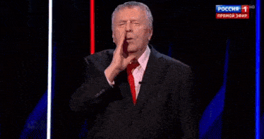 a man in a suit and tie laughs in front of a screen that says russia 1
