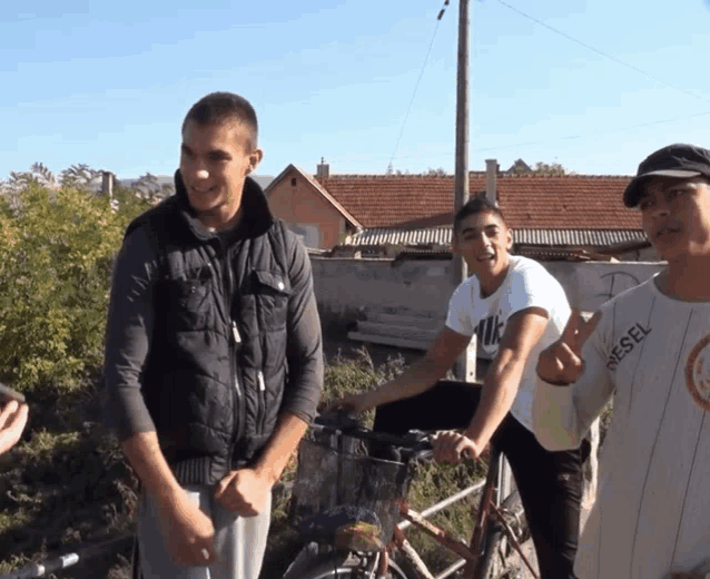 a man wearing a diesel shirt stands next to a man riding a bike