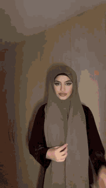 a woman in a hijab is standing in front of a wall .