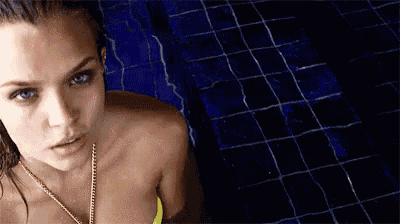 a woman in a yellow bikini is standing in a pool looking at the camera .