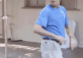 a man in a blue shirt and white pants is dancing in front of a window .