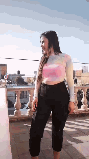 a woman is standing on a balcony wearing a pink crop top and black pants .